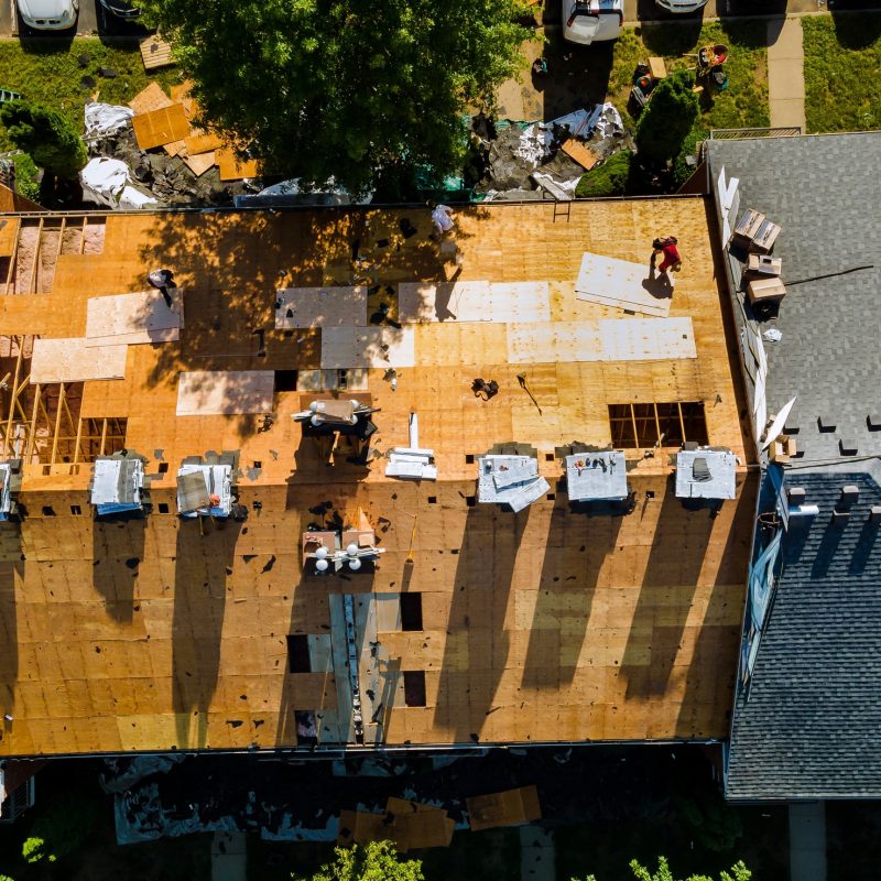A worker replace shingles on the roof of a home repairing the roof of a home A worker replace shingles on the roof of a home repairing the roof of a home