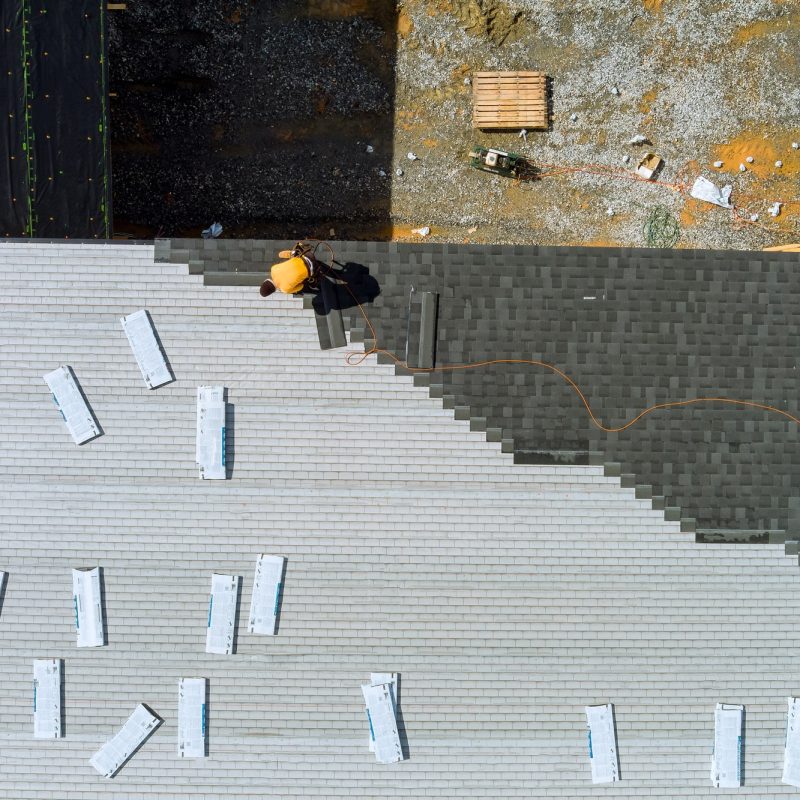 Roofer hands installing asphalt shingles on house construction roof with hammer and nails Roofer hands installing asphalt shingles on house construction roof with hammer and nails